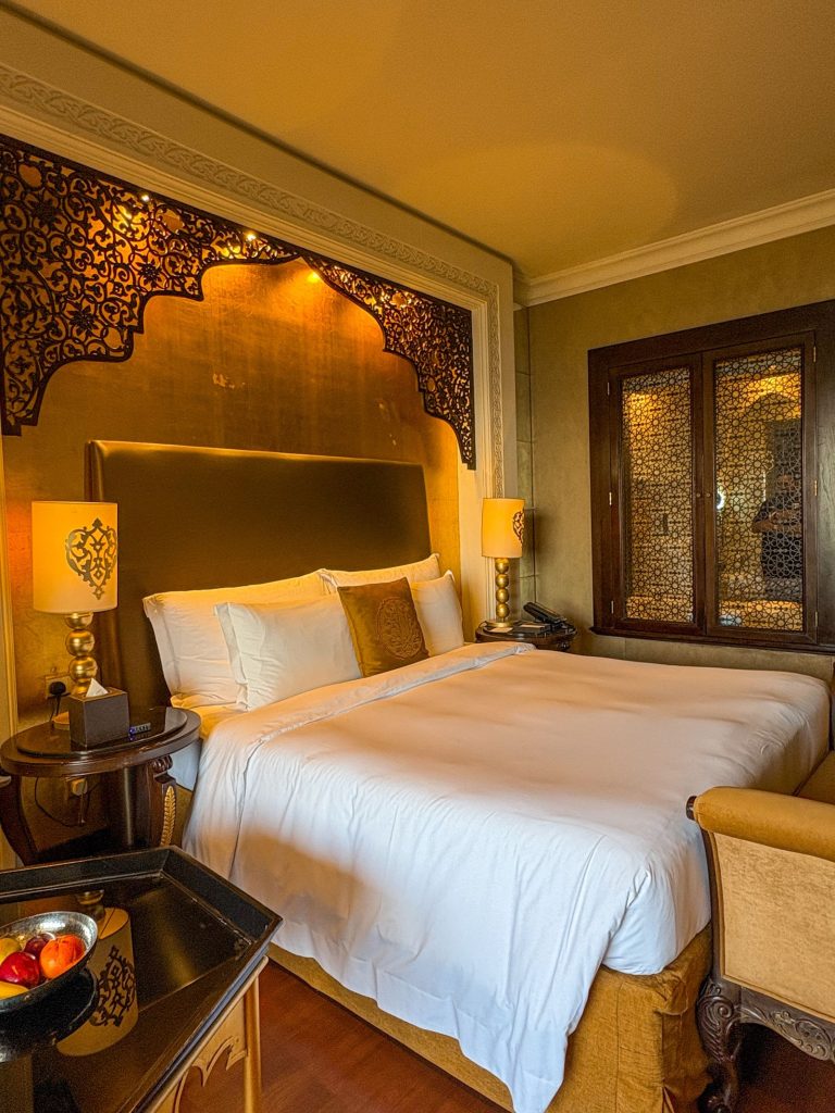 Hotel guest room fitted out with a carved cedar arch, brass-lattice doors, bedside furniture and lamps
